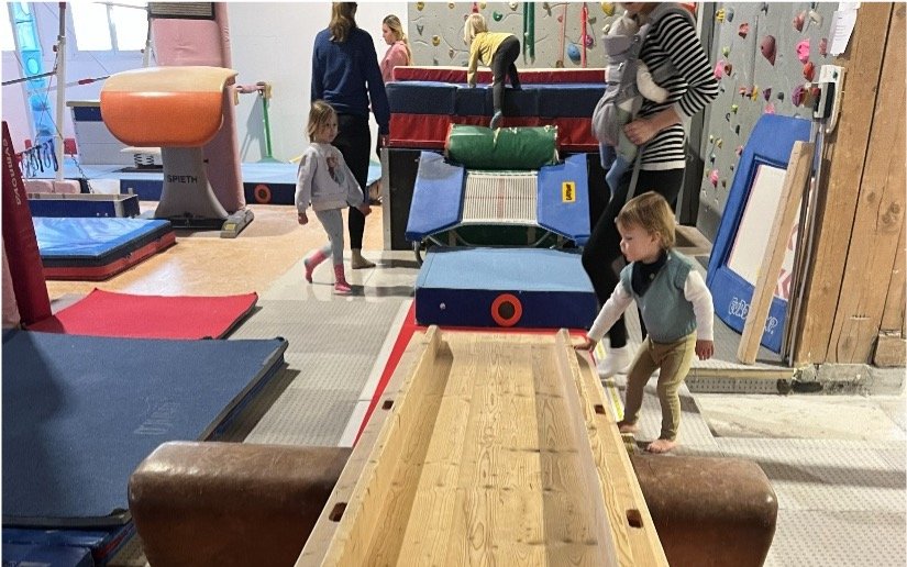 Kleinkinder erkunden Geräte im Krabbel Gym in Begleitung der Eltern